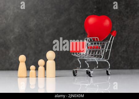 Quatre petites figurines en bois représentant une famille - mère, père et deux enfants - près d'une épicerie avec un grand coeur rouge. Concept d'amour familial Banque D'Images