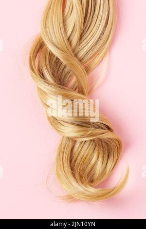 Cheveux longs et blonds courbés dorés. Une partie de cheveux blonds vue sur le dessus sur fond rose. Banque D'Images