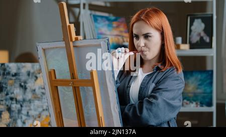 Portrait pensive rouge-cheveux caucasien femme peint dans la pièce penser à l'idée créer l'image ponder penser dessiner hobby talentueuse fille peindre dessus Banque D'Images
