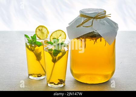 Pot de kombucha et deux verres de kombucha sont décorés de menthe, de citron et de raisins secs sur une table en béton gris clair. Boisson gazeuse fermentée sur un Banque D'Images