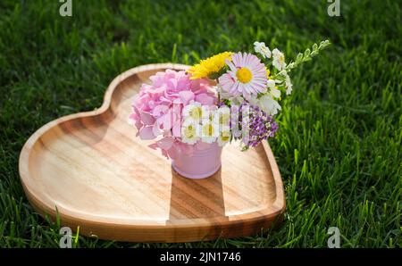 mini bouquet de fleurs de différentes couleurs dans un petit seau en métal se dresse sur une planche en bois en forme de coeur. Bonjour été. Félicitations, décl Banque D'Images