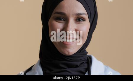 Souriant musulman arabe femme médecin chirurgien dans hijab traditionnel foulard porter un manteau médical regardant devant la caméra se tenant à l'hôpital Banque D'Images