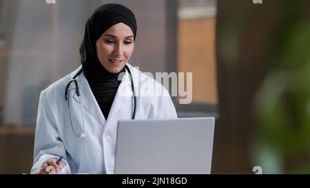 Femme arabe thérapeute médecin porter hijab manteau blanc appelant patient distant sur ordinateur portable parler avec le client dans la télé-télésanté télétéléphonique chat vidéo Banque D'Images