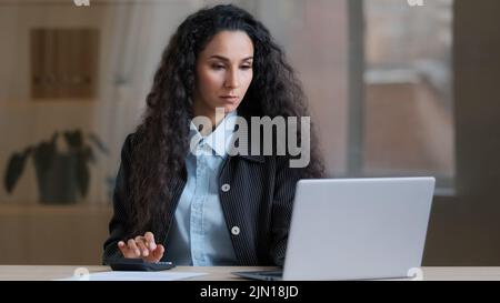 Femme d'affaires arabe concentrée travailleur multitâche comptable calculer les coûts solde de crédit utiliser ordinateur portable paiement en ligne e-commerce complet Banque D'Images