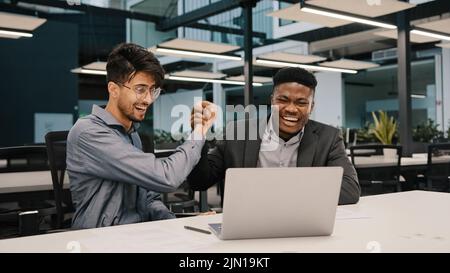 Partenaires masculins heureux divers hommes d'affaires collègues africains arabes regarder l'ordinateur portable se réjouir bonne nouvelle offre commerciale les hommes millénaires excités donner Banque D'Images