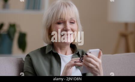 Mature âgés mature mature 60s femme caucasienne avec téléphone femme sourire utilise l'application mobile à la maison achète la médecine en ligne choisir des vêtements Internet shopping e- Banque D'Images