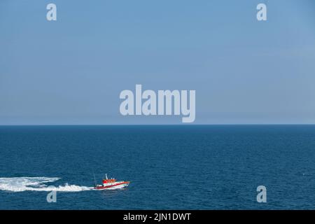Le bateau de recherche et de sauvetage flotte sur les vagues à grande vitesse. L'horizon est visible dans la distance. Ciel et mer. Arrière-plan bleu clair. Banque D'Images