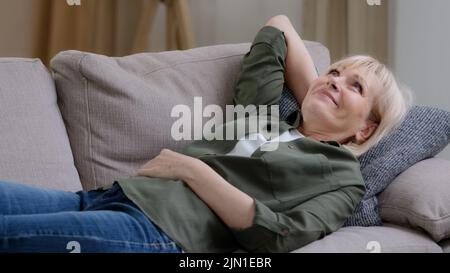 Heureuse femme rêveuse d'âge moyen et détendue. Reposez-vous sur un canapé à la maison. Ambiance paisible, calme et tranquille Banque D'Images