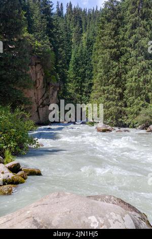 Une belle rivière de montagne orageux de teinte laiteuse coule rapidement entre de grandes pierres et des rochers près des montagnes et du ciel bleu. La rivière de montagne f Banque D'Images