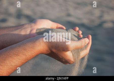 Sable qui coule à travers les doigts de la main d'un homme, sable du désert dans les dunes de Patara en Turquie Banque D'Images
