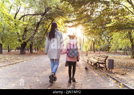 Maman et fille marchent dans le parc d'automne. Petite fille après l'école avec mère du dos. La vie quotidienne Banque D'Images