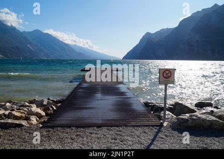 La ligne de plage pittoresque et une jetée en bois dans la ville méditerranéenne Riva del Garda sur le lac de Garde avec les montagnes en arrière-plan en Lombardie, Italie Banque D'Images