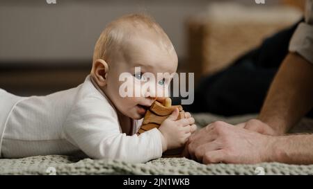 Famille caucasienne père méconnaissable Daddy jouer avec petite fille fils bébé nouveau-né tout-petit couché à la maison sur le sol avec des jouets bébé morsures en bois Banque D'Images