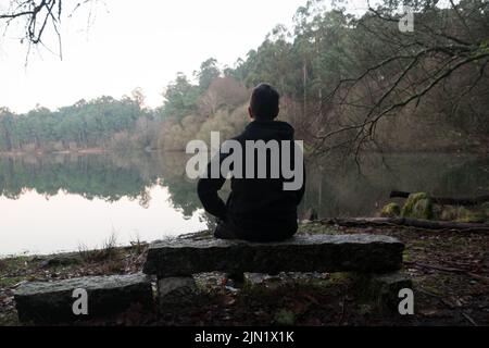 Homme assis sur un rocher en admirant la vue sur le lac dans la forêt Banque D'Images