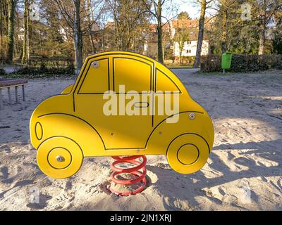 Une balançoire à ressort en forme de voiture stylisée sur une aire de jeux vide pour enfants avec un sol sablonneux Banque D'Images