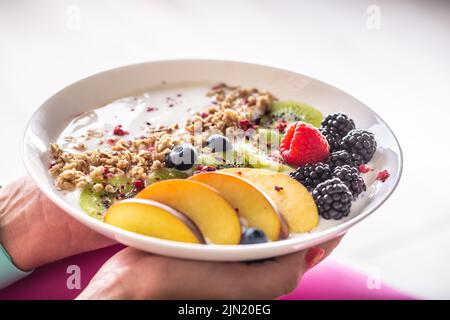 Yaourt, mûres muesli, framboises, bleuets, kiwis et pêches dans un bol blanc. Banque D'Images