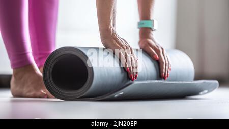 Une femme roule un tapis avant de pratiquer le yoga à la maison ou dans la salle de sport. Banque D'Images
