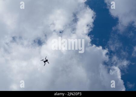 Silhouette de drone quadricoptère volant haut dans des nuages blancs sur ciel bleu, fond de ciel nuageux. Paysage de SkyScape Banque D'Images