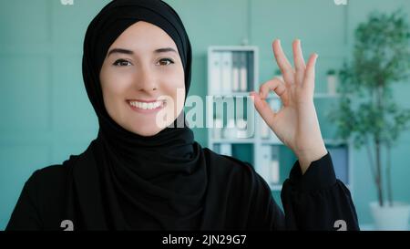 Portrait à l'intérieur musulmane islamique fille sourit en plein air à l'appareil photo montrant main ok signe. Une étudiante arabe féminine montre tout beau geste de réussite Banque D'Images