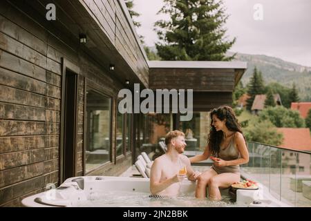 Un jeune couple attrayant appréciant dans le bain à remous extérieur en vacances Banque D'Images