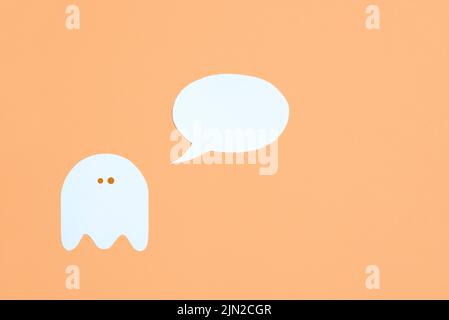 Design tendance minimaliste halloween, blanc mignon fantôme avec une bulle de parole vierge sur fond orange pastel, composition avec espace de copie. Banque D'Images