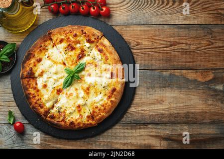 Une tranche de pizza italienne chaude avec du fromage étirant. Pizza quatre fromages avec basilic sur fond de bois. Vue de dessus avec espace de copie. Banque D'Images