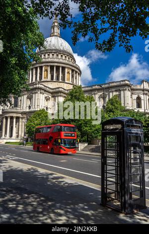 Londres, Royaume-Uni - 11 juin 2022 : cathédrale Saint-Paul, cabine téléphonique noire et bus à impériale rouge encadrés par des feuilles d'arbres Banque D'Images