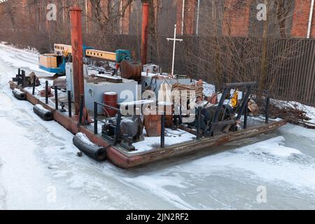 Une petite grue flottante et un bateau de service sont amarrés sur une rivière gelée à Saint-Pétersbourg, en Russie Banque D'Images