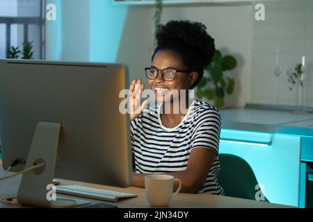 Jeune étudiante afro-américaine assise à table devant le pc tout en conversant en ligne. Banque D'Images