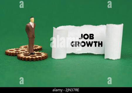 Concept d'entreprise. La figure d'un homme se tient sur les engrenages et lit l'inscription - Job Growth sur papier Banque D'Images