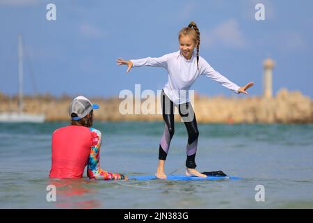 les jeunes surfeurs apprennent à monter à bord avec un instructeur à l'école de surf. Mode de vie actif en famille, leçons de sports nautiques pour les enfants Banque D'Images