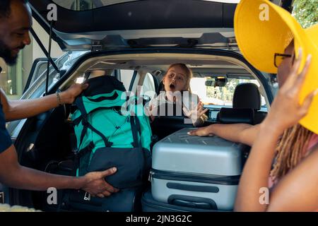 Un petit enfant et un mélange de personnes se rendant en vacances, chargeant des sacs de voyage dans le coffre du véhicule. Partez en vacances avec votre famille et vos amis, en mettant votre valise ou votre chariot en voiture avant le voyage. Banque D'Images