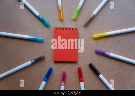 Bloc-notes pour notes avec feuilles rouges. Espace vide pour les notes. MOCAP. Sur fond kraft ocre chaud. Petit ordinateur portable à ressort reposant sur une table surroun Banque D'Images