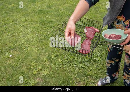 Les mains des femmes préparent des steaks de bœuf crus pour la friture sur le gril. Banque D'Images