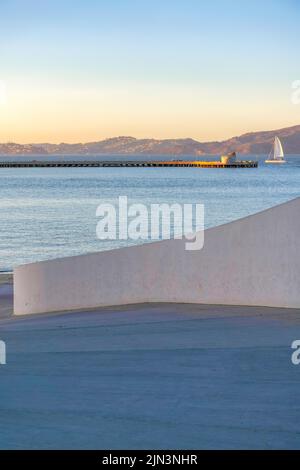 Vue sur un quai avec voilier sur le côté pendant le coucher du soleil à Fisherman's Wharf à San Francisco, CA. Il y a une chaussée et un mur en béton à l'avant A. Banque D'Images