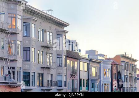 Maisons victoriennes et italianates dans la ville de San Francisco, Californie. Rangée de maisons aux tons violets, fenêtres à volets réfléchissants et stai d'urgence Banque D'Images