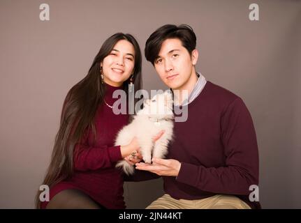 Jeune couple biracial attrayant posant avec un chiot blanc pomeranien de race pure Banque D'Images