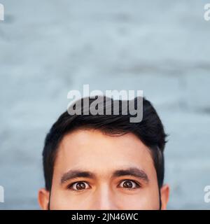 Je vous regarde. Portrait court d'un jeune homme face peeking de dessous contre un mur de brique. Banque D'Images