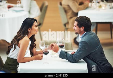 C'est un jeune couple affectueux qui tient les mains tout en étant assis à une table dans un restaurant. Banque D'Images