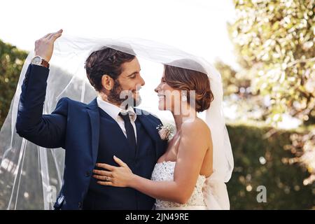 Je suis maintenant le vôtre et vous le mien. Un jeune couple affectueux et nouveau venu se souriant les uns les autres tout en se couvrant d'un voile sur leur mariage Banque D'Images