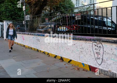 Londres, Royaume-Uni, 8th août 2022. Une femme passe devant le mur à l'extérieur des studios d'Abbey Road, couverte de messages des fans des Beatles. Il y a cinquante-trois ans, le matin du 8th août 1969, le photographe Iain Macmillan a pris des photos du groupe qui traversait le passage de zèbre, près du studio d'enregistrement, créant ainsi l'image emblématique de son album Abbey Road. Crédit : onzième heure Photographie/Alamy Live News Banque D'Images