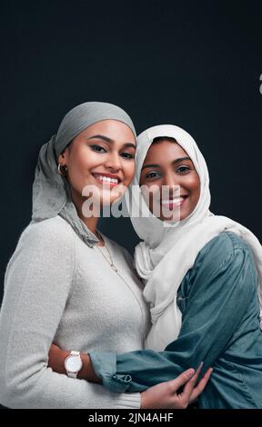 Nous avons beaucoup d'amour l'un pour l'autre. Deux jeunes femmes attrayantes portant des hijabs et s'embrassant l'une contre l'autre sur un fond noir dans le studio. Banque D'Images