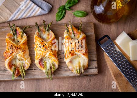Asperges vertes cuites au jambon et au fromage dans une pâte feuilletée parsemée de graines de sésame et de feuilles de basilic vert. Banque D'Images