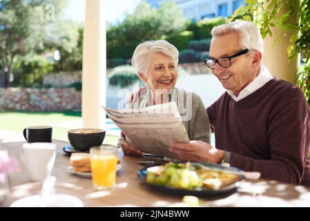 C'est ainsi que nous nous gardons dans la boucle. Un couple affectueux senior lisant le journal tout en appréciant un repas ensemble à l'extérieur. Banque D'Images