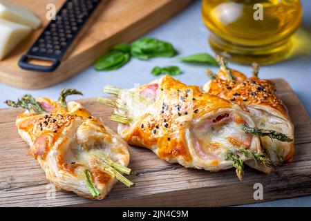 Asperges vertes cuites au jambon et au fromage dans une pâte feuilletée parsemée de graines de sésame et de feuilles de basilic vert. Banque D'Images