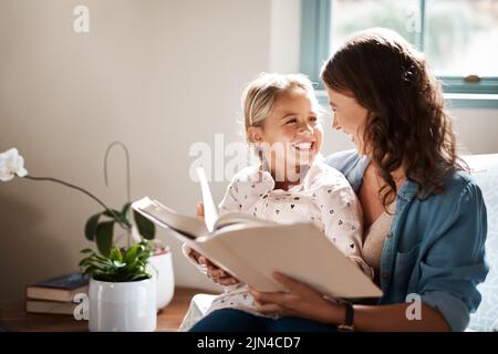 Maman fait l'apprentissage pour lire amusant. Une adorable petite fille lisant un livre avec sa mère sur le canapé à la maison. Banque D'Images