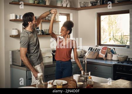 Vous me faites une fête. Un jeune couple affectueux dansant ensemble dans leur cuisine à la maison. Banque D'Images