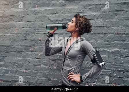 Rester hydraté pendant un entraînement. Une jeune femme prenant une pause-eau tout en faisant de l'exercice à l'extérieur. Banque D'Images