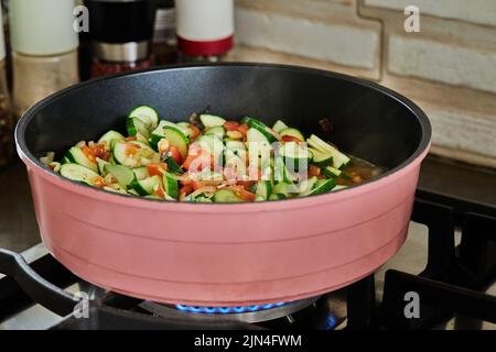 Les courgettes coupées en demi-anneaux avec des tomates sont frites dans la poêle, sur le poêle à gaz Banque D'Images
