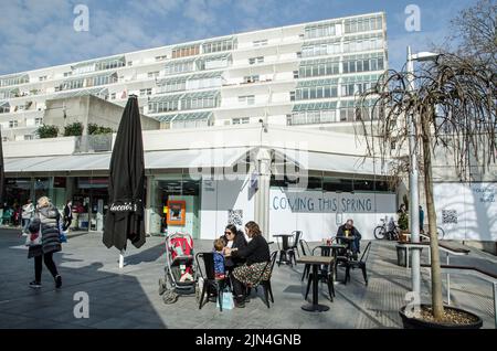 Londres, Royaume-Uni - 21 mars 2022 : les clients qui profitent du soleil aux tables de café se trouvent au Brunswick Centre à Bloomsbury, dans le centre de Londres. Le brutal Banque D'Images